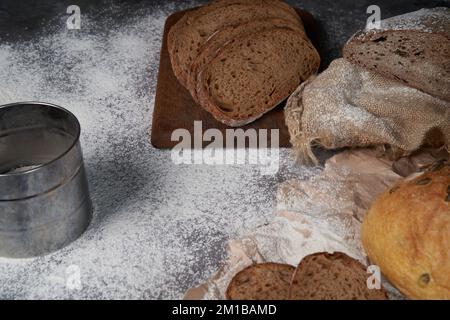 Vista dall'alto di vari tipi di pane, affettato e intero, farina, carta stropicciata e tela di tela su un tavolo di legno. Angolo alto. Foto Stock