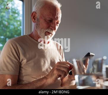 Uomo maturo che digita sul telefono cellulare al tavolo al chiuso Foto Stock