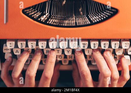 Primo piano delle mani sulla macchina da scrivere arancione vintage. Scrittore letterario Foto Stock