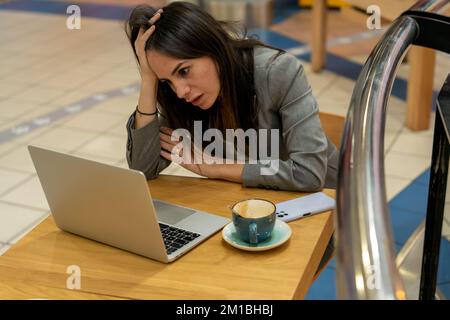 Dall'alto di stanco rovesciato imprenditore femminile con lunghi capelli scuri in abito di classe che tocca la testa mentre si siede a tavola e leggendo cattive notizie Foto Stock