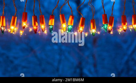 Luci di Natale sulla finestra al crepuscolo e alberi coperti di neve all'esterno Foto Stock
