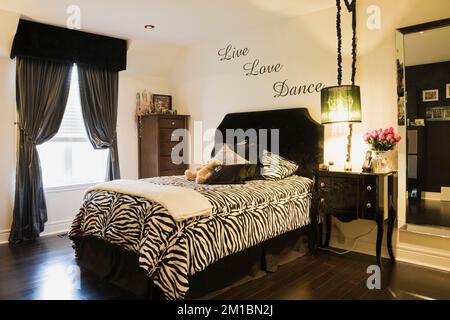 Letto singolo con motivi zebrati, copriletto e comodino nella camera da letto dei teenager all'interno di una casa lussuosa. Foto Stock