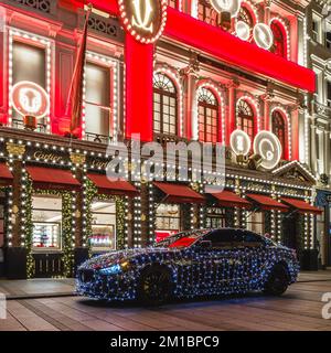 Un'auto di lusso illuminata fuori dall'iconico negozio Cartier di Londra durante la stagione natalizia. Foto Stock