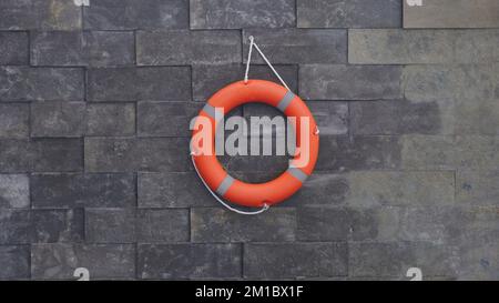 salvagente arancione appeso alla parete di pietra della piscina. sicurezza per le persone in acqua Foto Stock