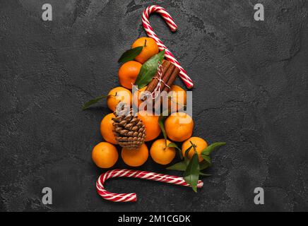 Albero di Natale fatto di tangerini freschi, foglie, canne caramelle e cannella su fondo scuro Foto Stock