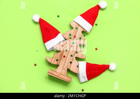 Composizione con cappelli di Santa e albero di Natale in legno su sfondo verde Foto Stock