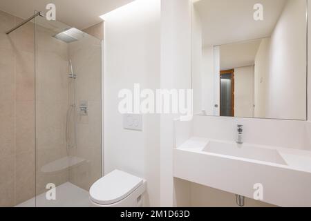 Bagno spazioso e luminoso dal design minimalista con tutto ciò di cui hai bisogno. Lavabo costruito in un bancone in marmo bianco neve con un grande specchio Foto Stock