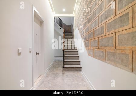 Scala in pietra con ringhiera in legno che conduce al secondo piano in un corridoio luminoso. Corridoio alla moda, moderno e chiaro, con porta bianca e finiture decorative Foto Stock