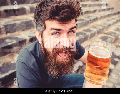 Ragazzo che si riposa con la birra alla spina. Hippster su allegro sorriso viso drink birra all'aperto. L'uomo con barba e baffi tiene il bicchiere con la birra mentre siede Foto Stock