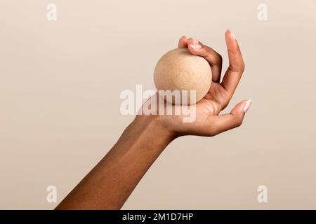 Crop anonimo afro-americana femmina che mostra una piccola palla di legno rotonda su sfondo beige Foto Stock