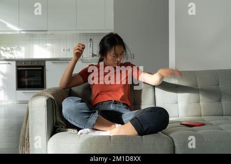Giovane donna asiatica distratta buttando via smartphone, ricevendo testo di rottura dal ragazzo Foto Stock