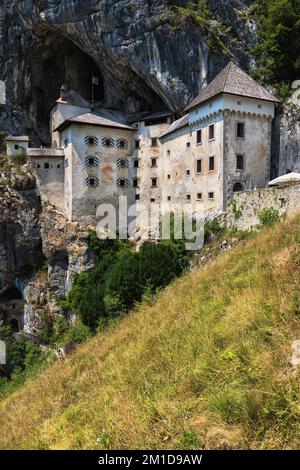 Paesaggio con il Castello di Predjama in Slovenia. Castello medievale grotta in scogliera con rete di tunnel segreti e prato sul pendio di montagna. Foto Stock