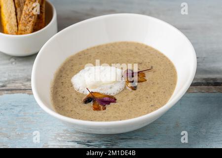 Crema di zuppa di funghi in ciotola di porcellana bianca su tavolo di legno Foto Stock