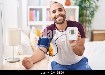 Giovane uomo latino che misura l'impulso usando il tensiometro in camera da letto Foto Stock
