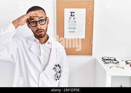 L'uomo ottico afro-americano in piedi dalla prova della vista preoccupato e sottolineato circa un problema con la mano sulla fronte, nervoso e ansioso per crisi Foto Stock
