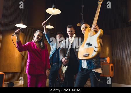 Membri della band felici con i loro strumenti. Donna caucasica in piedi con batterista e chitarristi caucasici. Foto di alta qualità Foto Stock