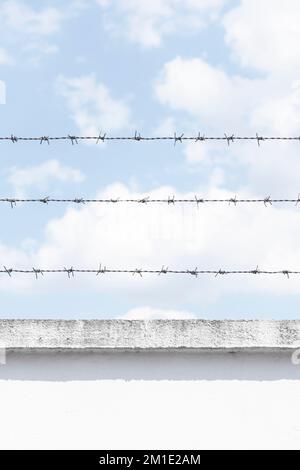 Filo spinato un tipo di filo di recinzione in acciaio costruito con bordi affilati sulla parte superiore di una parete di prigione contro il cielo blu chiaro Foto Stock