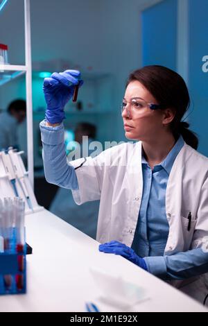 Scienziato che tiene campione di sangue vacutainer in laboratorio sanitario. Ricercatore in laboratorio di medicina chimica che lavora con apparecchiature tecnologiche professionali per lo sviluppo sanitario. Foto Stock