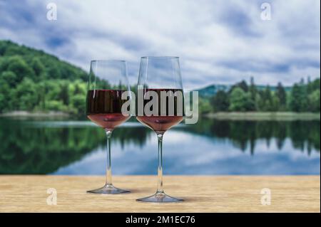 Due bicchieri di vino rosso con lago sullo sfondo di una foresta. Foto Stock