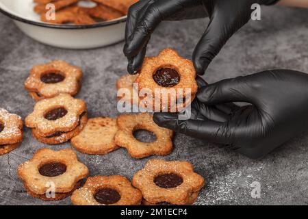 Biscotti natalizi Linzer. Il confetter con guanti riempie i biscotti con marmellata di prugne. Dolci fatti in casa Foto Stock