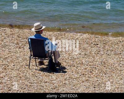L'uomo si è seduto da solo sulla spiaggia guardando sopra il Solent, Hill Head Beach, Lee-on-the-Solent, Hampshire, Regno Unito Foto Stock