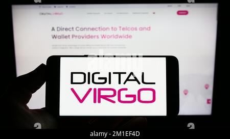 Persona che tiene il cellulare con il logo della società di pagamento francese Digital Virgo S.A. sullo schermo di fronte al sito web aziendale. Messa a fuoco sul display del telefono. Foto Stock
