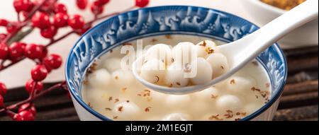 Piccolo tangyuan bianco (tang yuan, palle di gnocchi di riso glutinoso) con miele di osmanthus dolce e zuppa di sciroppo in una ciotola su fondo di tavolo di legno. Foto Stock