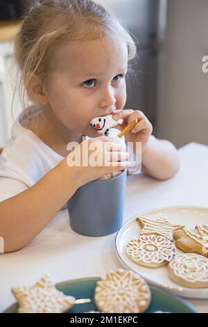 I bambini piccoli e carini mangia un pupazzo di neve di marmello decorato con glassa e beve cacao. Foto Stock