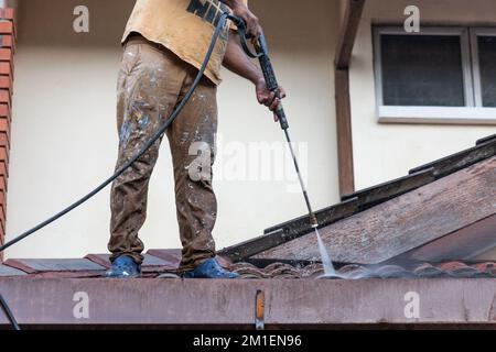 Lavoratore che utilizza una pistola a spruzzo ad acqua ad alta pressione per lavare e pulire lo sporco dalle piastrelle del tetto durante i lavori di ristrutturazione Foto Stock