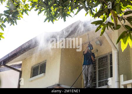 Lavoratore che utilizza una pistola a spruzzo ad acqua ad alta pressione per lavare e pulire la sporcizia dal soffitto del tetto Foto Stock