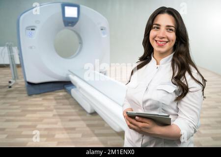 Medico con un tablet digitale sorridente e guardando la fotocamera sullo sfondo di uno scanner TC Foto Stock