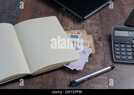 Frammento di libro contabile di un dispositivo di conto con banconote in euro e una penna stilografica sullo sfondo di un tavolo di legno. Foto Stock