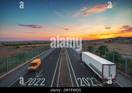 Guida su strada aperta verso il nuovo anno 2023 al tramonto. Vista aerea dell'autostrada, dell'auto, del furgone e del camion. Trasporto, logistica, concetto di viaggio Foto Stock