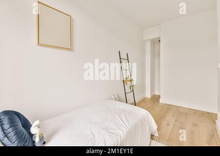una camera da letto con pareti bianche e pavimento in legno, compresa una scala appoggiata alla parete accanto al letto Foto Stock