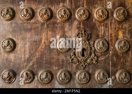 Porta medievale in legno con decorazioni in bronzo intagliato con leoni e toppa con decorazione a corona in primo piano. Foto Stock