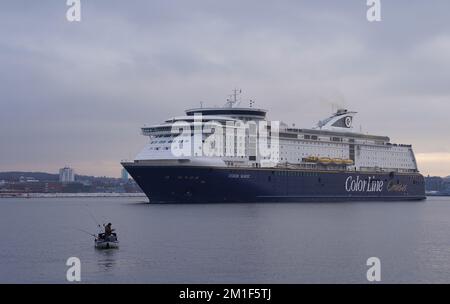 12 dicembre 2022, Schleswig-Holstein, Kiel: Un pescatore sta pescando sul fiordo di Kiel mentre il traghetto della linea di colore lo passa per il Mar Baltico. Foto: Marcus Brandt/dpa Foto Stock