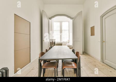Semplice tavolo con sedie situato sotto un elegante lampadario vicino alle porte in un'elegante sala da pranzo Foto Stock
