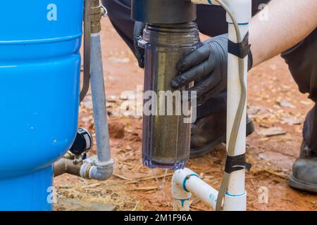 Un operatore professionale esegue la manutenzione delle apparecchiature, inclusa la sostituzione dei filtri sostituibili per l'acqua all'esterno vicino alla casa Foto Stock