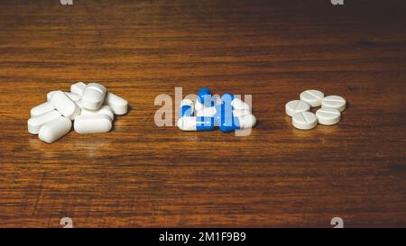 Un semplice mucchio di pillole bianche e blu, medicine, pillole impilate su un tavolo marrone. Concetto medico. Foto Stock
