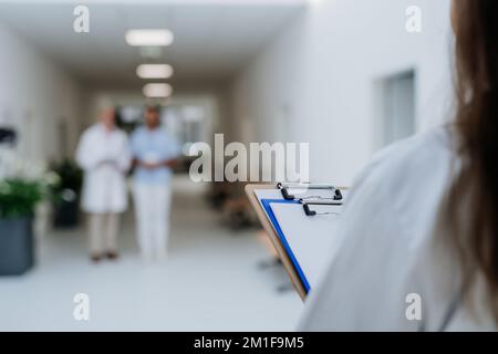 Vista posteriore del giovane medico con cartella clinica in attesa di colleghi più anziani. Foto Stock