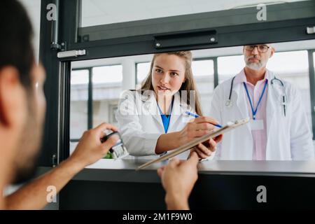 Giovane medico che parla alla reception dell'ospedale con la sua collega. Foto Stock