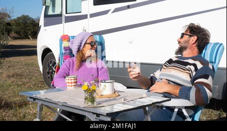 Uomo e donna che si divertono e si rilassano insieme fuori dal loro veicolo camper seduto al tavolo e parlando con risate. Buon punto di interesse turistico Foto Stock