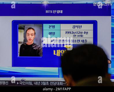 Jin, un membro del gruppo K-pop BTS, sta mostrando un'immagine del suo taglio di capelli e la notizia del suo arruolamento nell'esercito sudcoreano prima del suo arruolamento nell'esercito in TV alla stazione ferroviaria di Yongsan a Seoul. Jin, il membro del gruppo K-pop BTS per servire in esercito, ha rilasciato una foto di sé con un taglio militare di capelli prima del suo arruolamento. Il 13 dicembre, secondo fonti militari e industriali, il cantante di 30 anni entrerà in un campo di stivali di una divisione in prima linea Army 5 a Yeoncheon, 60 chilometri a nord di Seoul. Dopo un programma di formazione di base di cinque settimane, Jin sarà Foto Stock