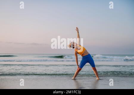 Giovane donna che fa esercizi in spiaggia, routine mattutina e concetto di stile di vita sano. Foto Stock