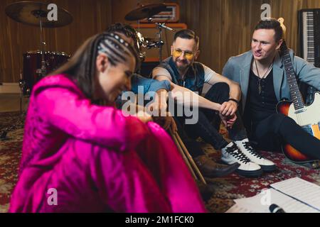 due chitarristi, un batterista e un cantante sul pavimento che discutono della loro nuova canzone in studio. Foto di alta qualità Foto Stock