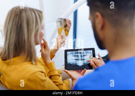 Vista posteriore del dentista che mostra la scansione radiografica sul tablet digitale al paziente. Foto Stock