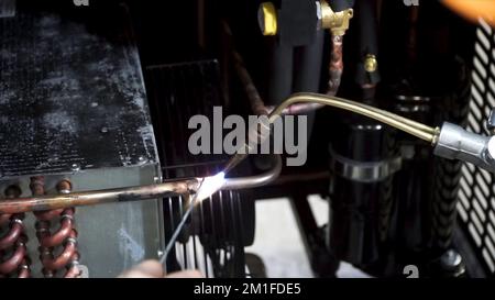 Un operatore utilizza il bruciatore a gas e la saldatura per saldare tubi in rame. Dettagli riscaldatori bruciatore di lavoro. Metal worker in una fabbrica che utilizza una burne di pista Foto Stock