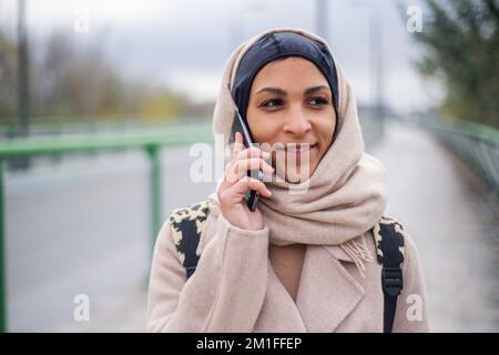 Ritratto di una giovane donna musulmana che cammina e chiama in una città. Foto Stock