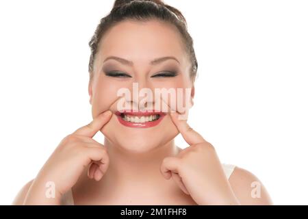 Giovane donna cubby costringendo il suo sorriso con le dita su sfondo giallo. Foto Stock