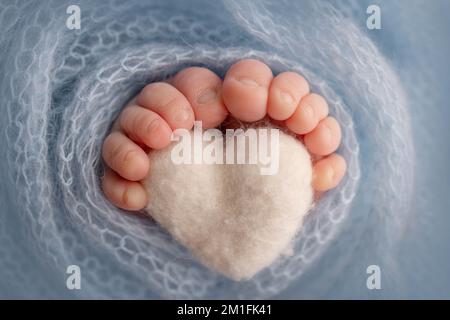 Gambe, dita dei piedi e talloni di un neonato. I piedi avvolti in una coperta a maglia blu. Macro stidio foto, primo piano. Cuore blu lavorato a maglia nelle gambe del bambino. Foto Stock